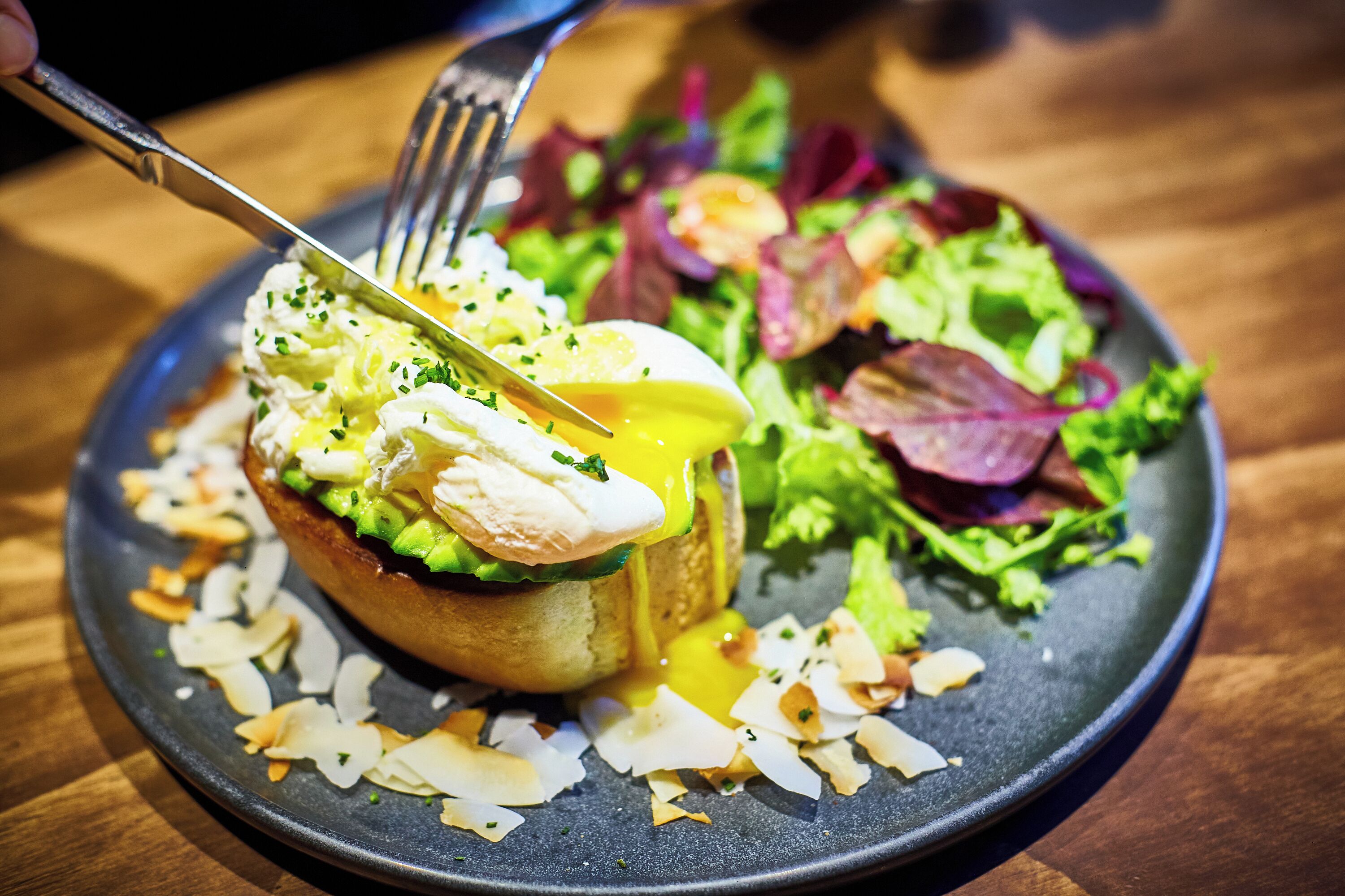 A plate with a poached egg, avocado, and greens, with a fork on the side.