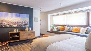 Une chambre moderne avec un grand lit, une commode en bois, un tableau au mur et une fenêtre donnant sur un beau paysage.