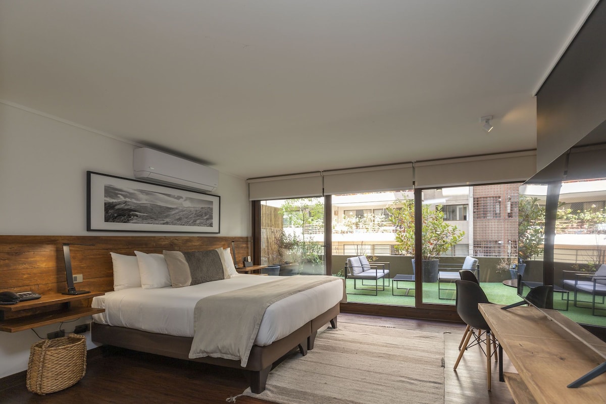 A bedroom with a bed, bedside table, lamp, and a view of the outdoor area.