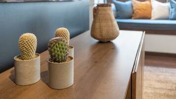 A wooden table with three potted cacti and a vase in a modern living room with a blue wall and a sofa with cushions.