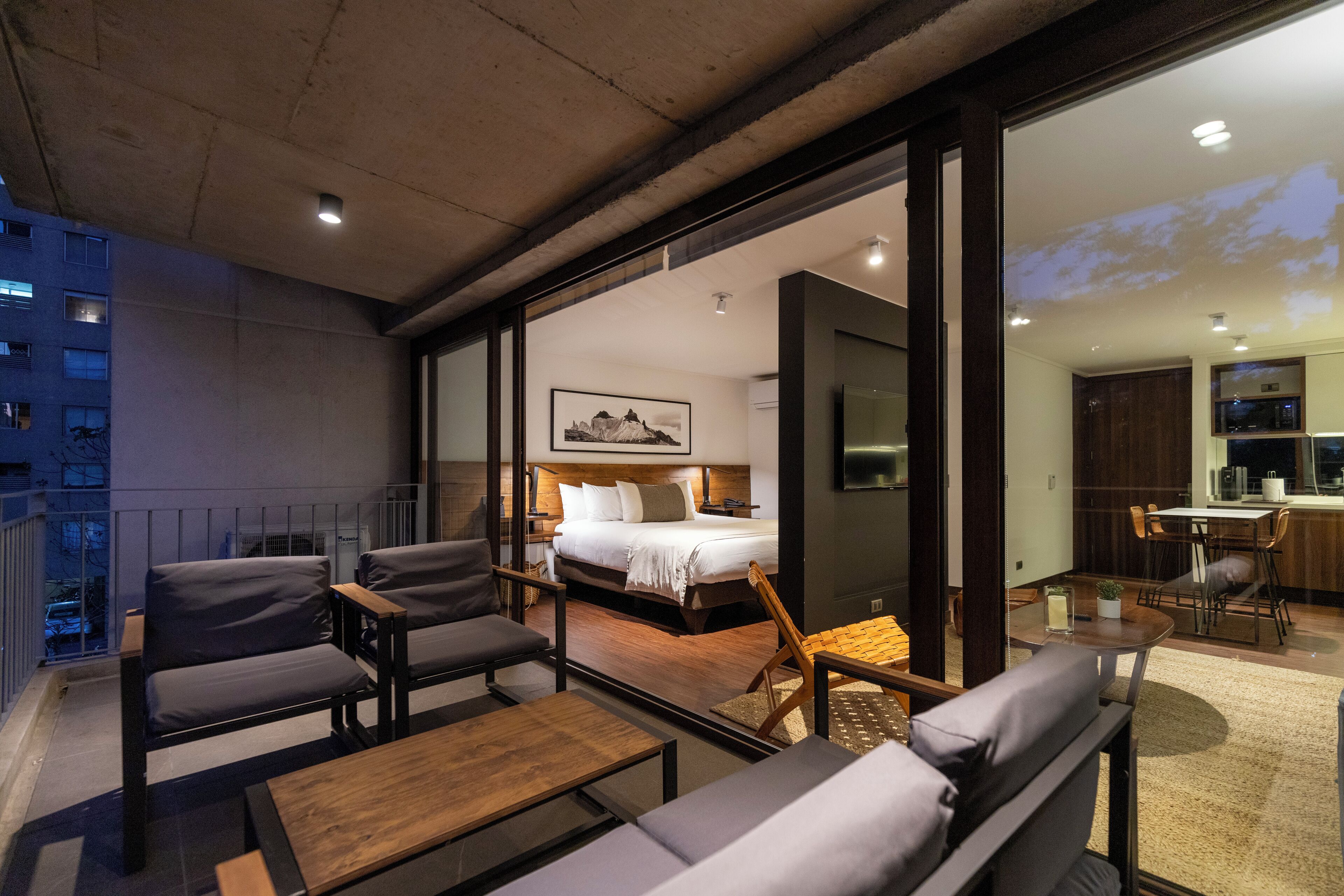 A modern hotel room with a large bed, a desk, and a balcony with seating.