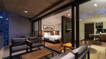 A modern hotel room with a large bed, a desk, and a balcony with seating.