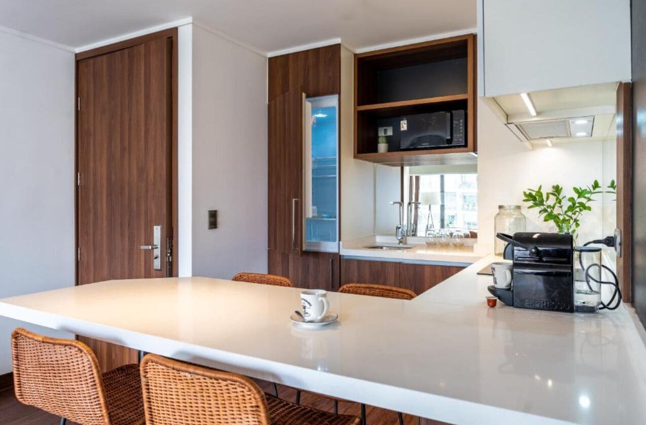 Une cuisine moderne dotée d’un îlot central, d’appareils électroménagers intégrés et de chaises en osier.