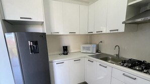 Une cuisine moderne avec des meubles blancs, un réfrigérateur en acier inoxydable, un four à micro-ondes, une machine à café et une cuisinière à gaz.