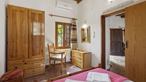 Quarto com guarda-roupa de madeira grande, penteadeira de madeira, uma cadeira e cama com roupa de cama rosa.