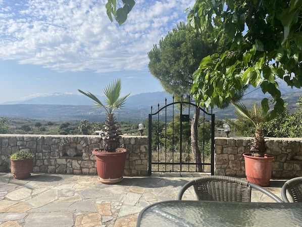 Une terrasse en pierre avec des plantes en pot, un portail en fer forgé et une vue sur les montagnes lointaines.