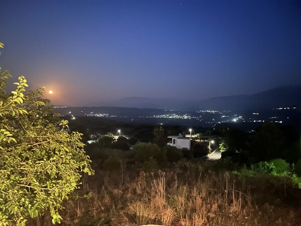A nighttime view of a town with distant lights, a moon, and a hill with a building. - Artemis House stone cottage in historic Aptera village, Chania (Aptera)