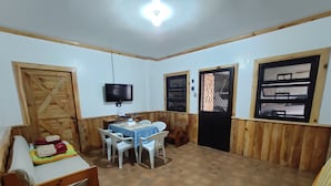A room with a wooden bed, a small table with chairs, a TV mounted on the wall, and a window with a wooden frame. - Log Homes Inspired Unit w/ Wi-Fi and Cable (Baguio)