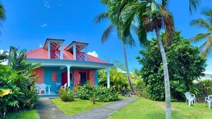 A two-story house with a red roof and a porch, surrounded by lush greenery and palm trees. - bungalows Cas'à Willy - Alamanda 3 (Sainte-Rose)