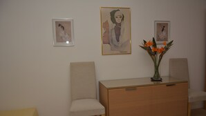 A room with a wooden cabinet, two chairs, and three framed artworks on the wall. - Atlantic view 1 - Apartment with ocean view & pool (Funchal)