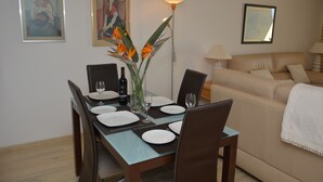 A dining area with a table set for four, a sofa, and two wall-mounted lamps. - Atlantic view 1 - Apartment with ocean view & pool (Funchal)