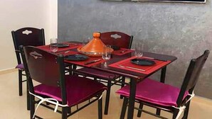 Comedor con una mesa dispuesta para cuatro personas, con sillas rojas y una maceta anaranjada en el centro.