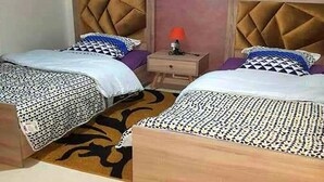 Habitación de hotel con dos camas, cada una con cabecero capitonado, mesita de noche con lámpara y colcha estampada.