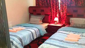 Een hotelkamer met twee bedden, elk met een blauw gestreepte dekbedovertrek en bijpassende kussens. Tussen de bedden staat een nachtkastje met een lamp.
