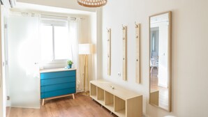 Une pièce lumineuse avec un plancher en bois, une commode bleue, un banc blanc et un grand miroir au mur.