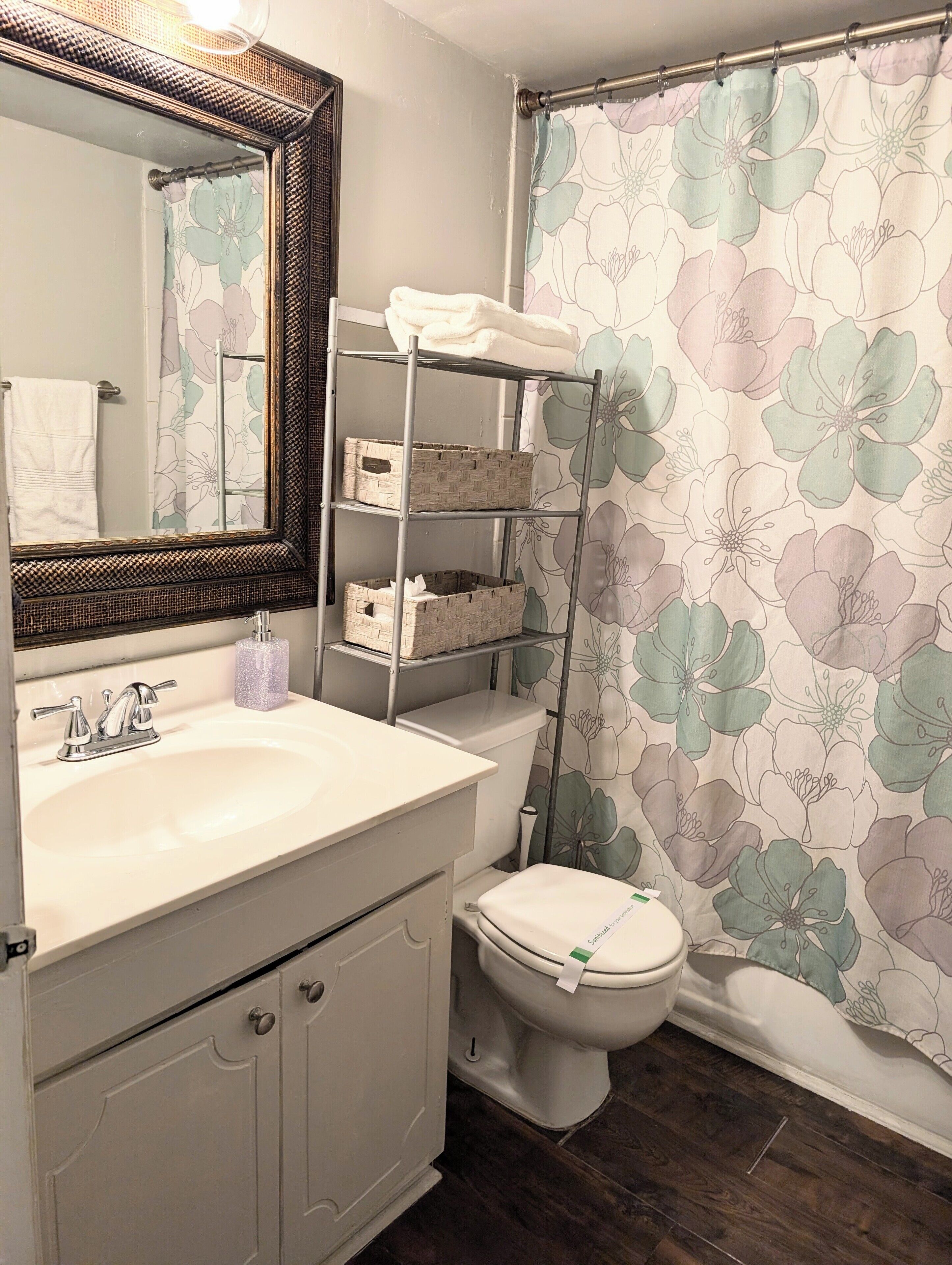 A bathroom with a white sink, a mirror with a decorative frame, a toilet, and a shower curtain with a floral pattern.