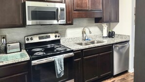 A kitchen with dark wooden cabinets, a stainless steel microwave, a stove, a sink, and a dishwasher. - Cozy  2bdr. Condo in Central Raleigh (Raleigh)