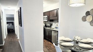 A modern kitchen with dark wood cabinets, stainless steel appliances, and a dining area with a glass table and white chairs. - Cozy  2bdr. Condo in Central Raleigh (Raleigh)