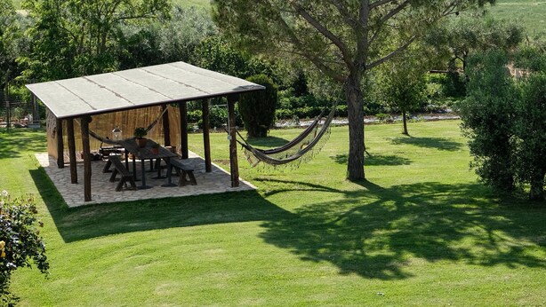 A gazebo with a picnic table and hammock in a grassy area with trees.