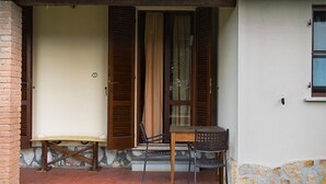 Un petit espace extérieur aménagé avec une table et des chaises, un mur en briques et une fenêtre avec des volets.