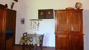 Un coin repas avec une table recouverte d’une nappe à motifs de tournesols, des chaises en bois, un buffet en bois sur lequel repose un globe terrestre, et une horloge murale.