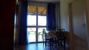 Ein Zimmer mit Esstisch und Stühlen, einer Glastür zu einem Außenbereich und einer geschlossenen Tür rechts.
