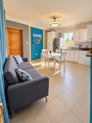 A modern living room with a sofa, dining table, and chairs. There is a kitchen area with cabinets and appliances. - Karimar Beach Condo Hotel (Punta Cana)