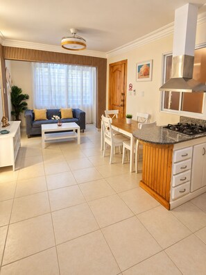 A modern living room with a sofa, coffee table, and a dining area with chairs and a kitchen island. - Karimar Beach Condo Hotel (Punta Cana)