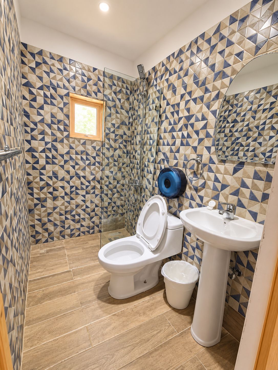 A bathroom with a geometric patterned tile wall, a white toilet, a pedestal sink, and a shower area.