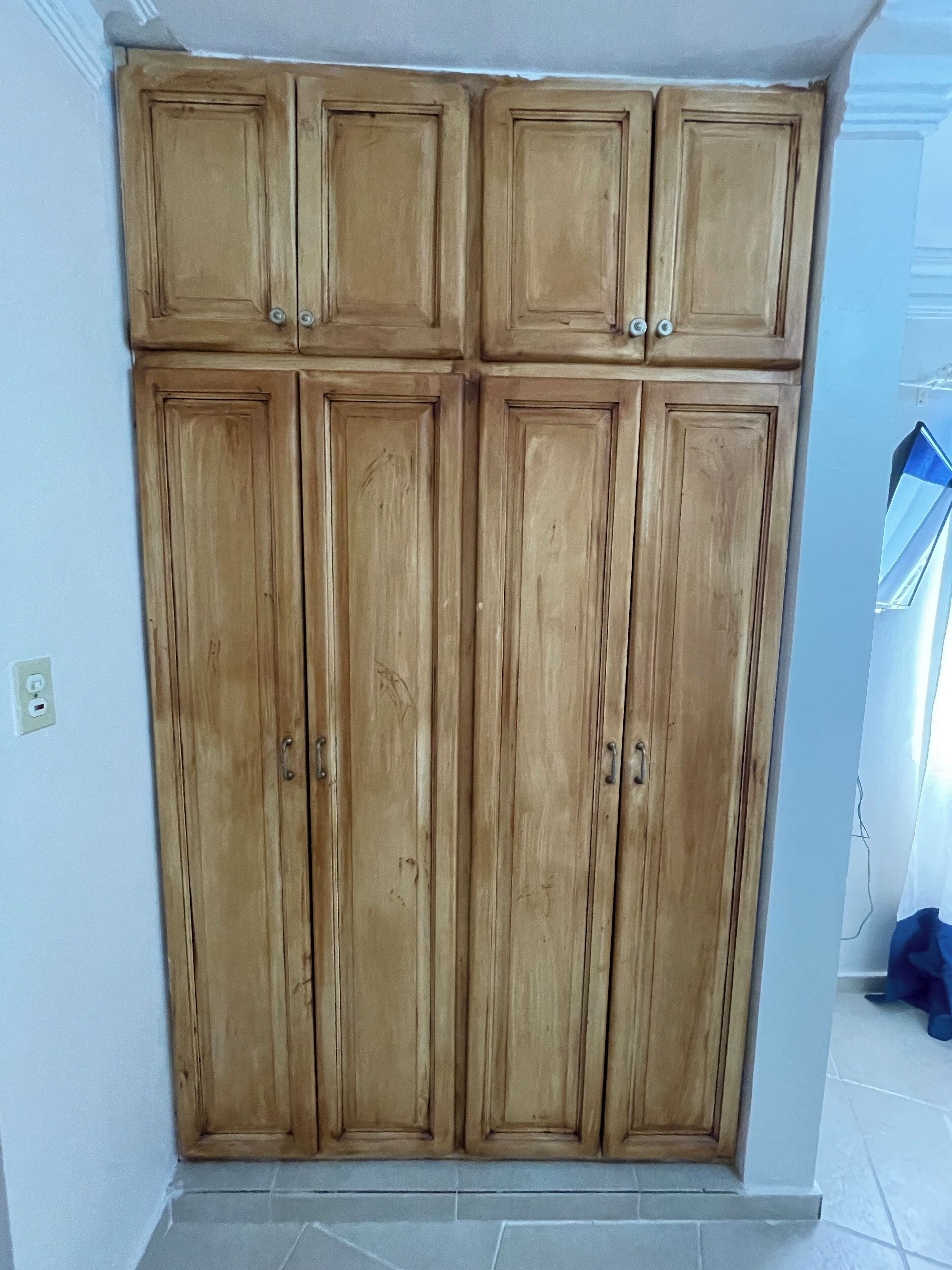 A large wooden wardrobe with multiple doors and handles, located in a room with tiled flooring and a white wall.
