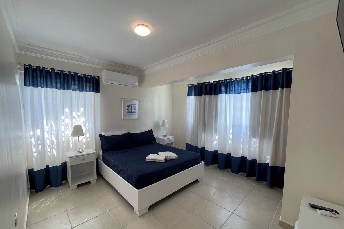A bedroom with a bed, nightstands, a lamp, and curtains.