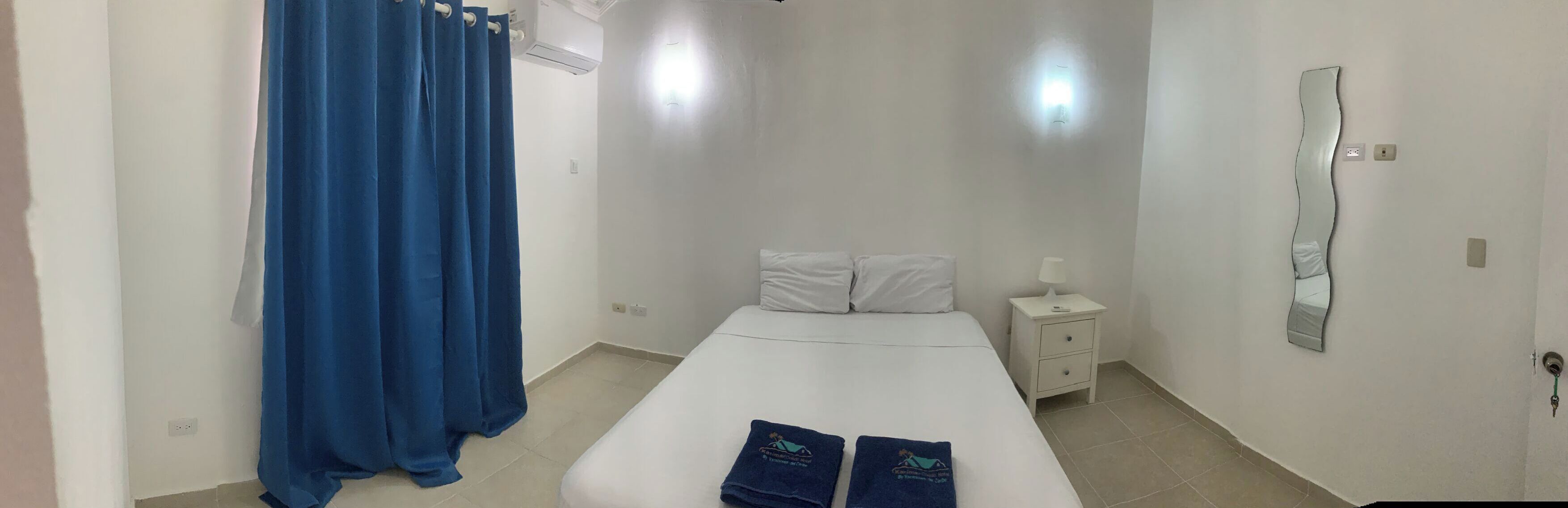 A hotel room with a single bed, a nightstand, a mirror, and a blue curtain.