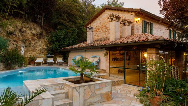 Una casa in pietra con piscina, area salotto esterna e giardino.