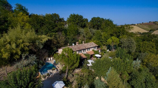 A villa with a swimming pool surrounded by dense trees and hills in the background. - Villa Agave 8, Emma Villas (Monteciccardo)
