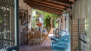 Un'area patio coperta con travi in legno rustico, mobili in vimini e pavimento in mattoni.
