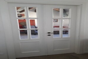 Een witte deur met een ruit, die een kamer onthult met een bed en een rode muur.