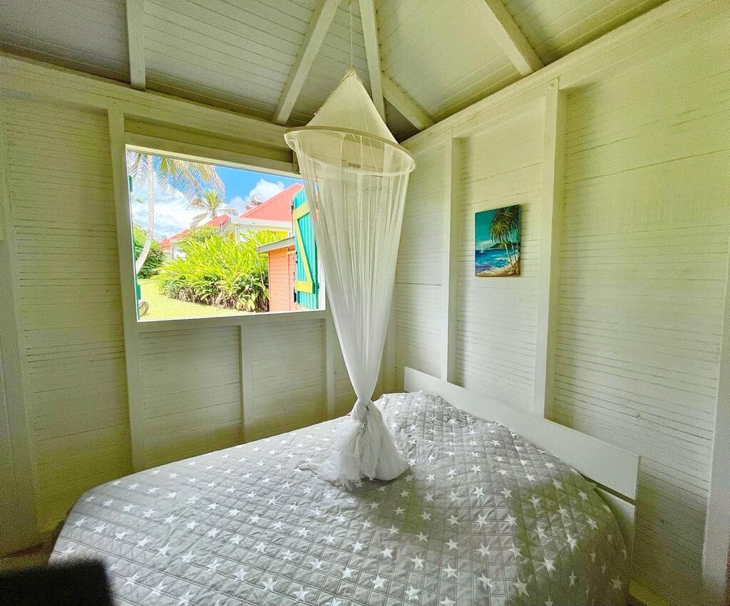 A room with a bed, a window with a view of greenery, and a painting on the wall.