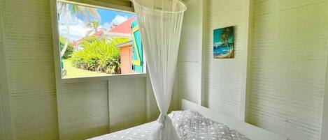 A room with a bed, a window with a view of greenery, and a painting on the wall.