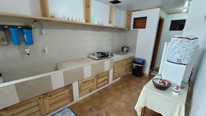 Une cuisine compacte avec un plan de travail en bois, un évier, une petite table avec un saladier et une fenêtre avec des stores.