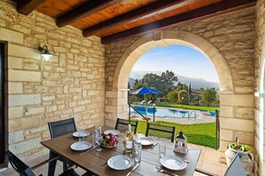 An outdoor dining area with stone walls, a wooden ceiling, and a view of a swimming pool and mountains. - Villa Maza, beautiful stone villa in traditional village Maza, Chania (Maza)