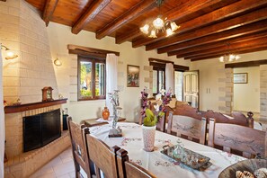 A dining area with a fireplace, wooden ceiling beams, and a table set for a meal.