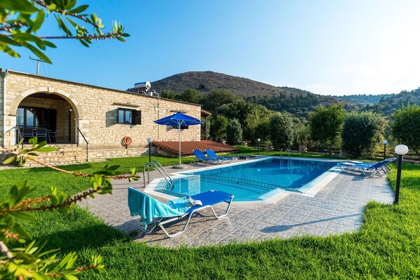 A stone building with a swimming pool, blue lounge chairs, and a mountain in the background. - Villa Maza, beautiful stone villa in traditional village Maza, Chania (Maza)