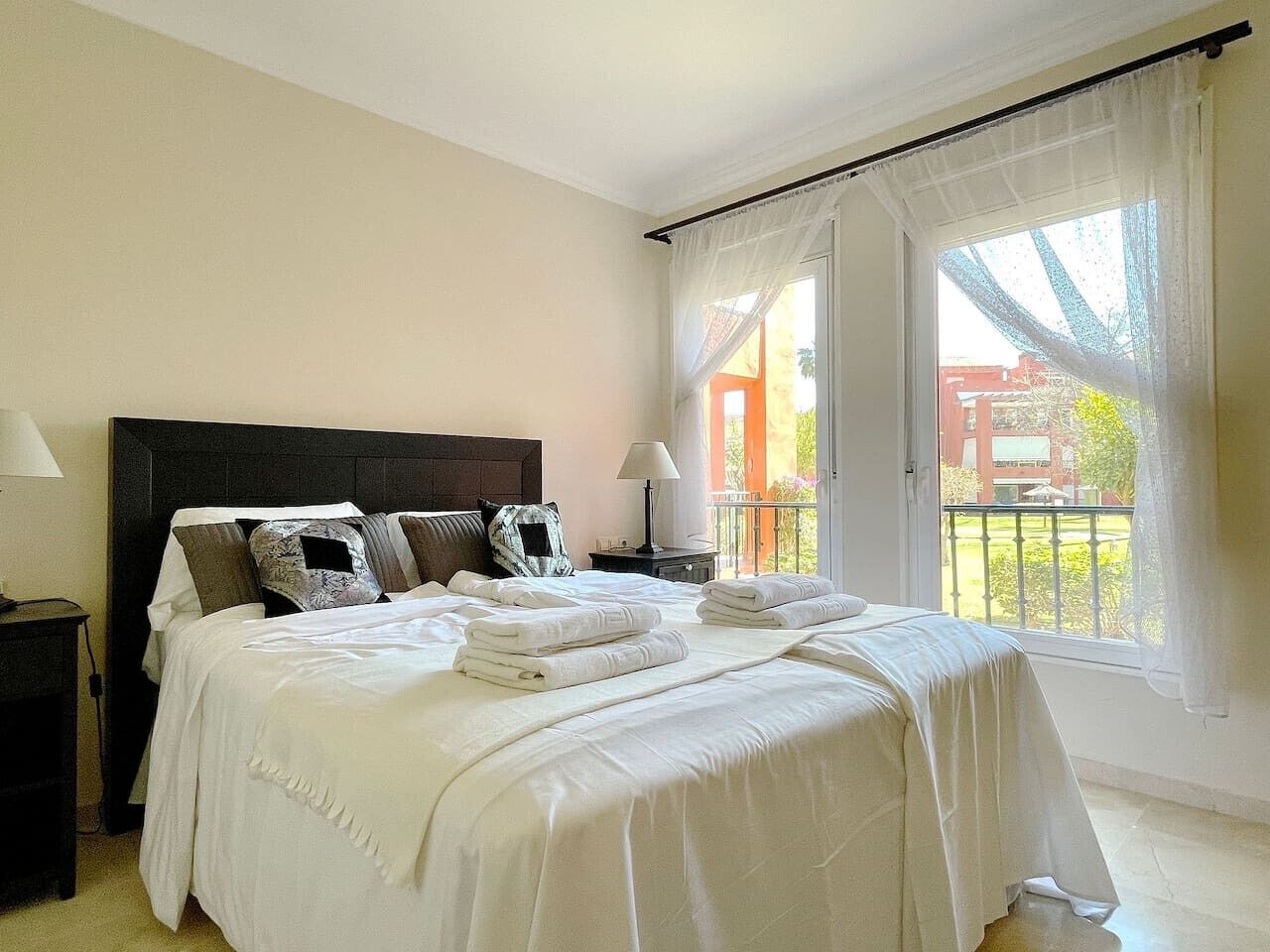 Une chambre avec un grand lit, une table de chevet, une lampe et une vue sur l’extérieur.