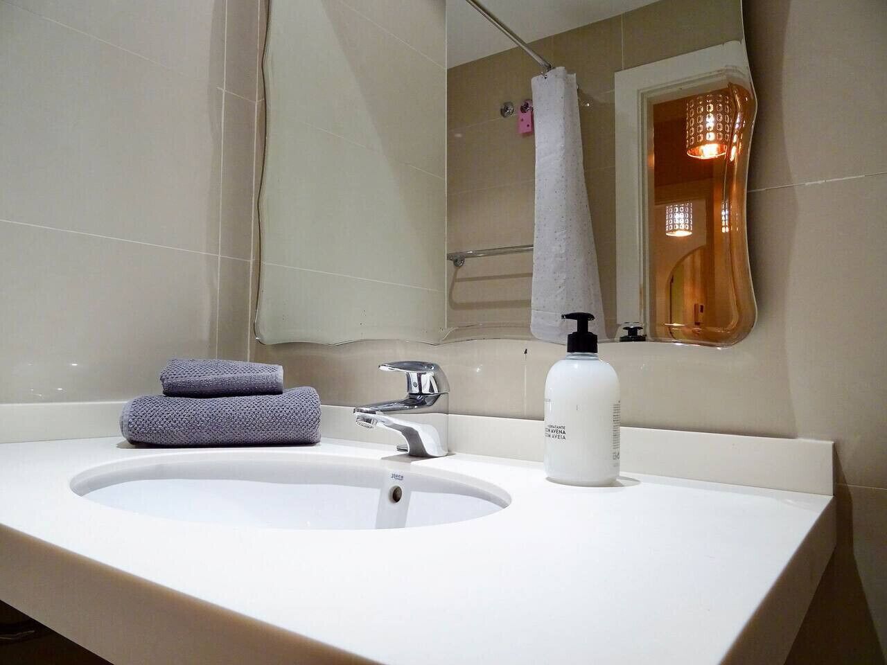 Een badkamer met een witte wastafel, een spiegel, een handdoek en een zeepfles.