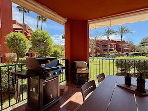 A patio with a grill, outdoor seating, and a view of a building with palm trees.