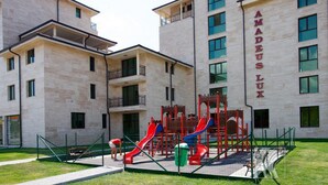 Un parque infantil con toboganes y estructuras para escalar frente a un edificio identificado como "AMADEUS LUX".