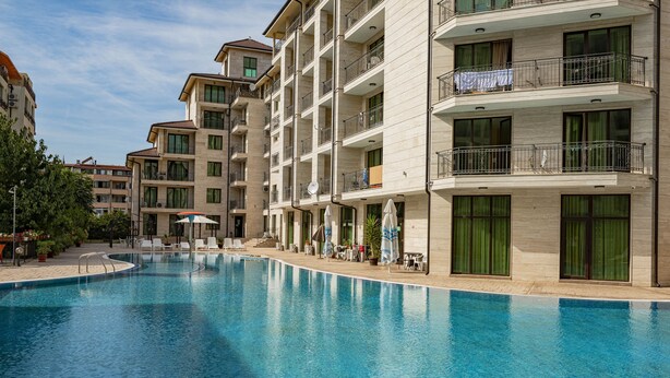 Una piscina rodeada de edificios de varios pisos con balcones, mobiliario exterior y plantas en macetas.