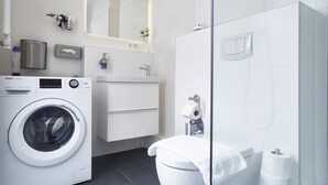 Ein modernes Badezimmer mit Waschmaschine, Toilette und einer Duschkabine aus Glas.