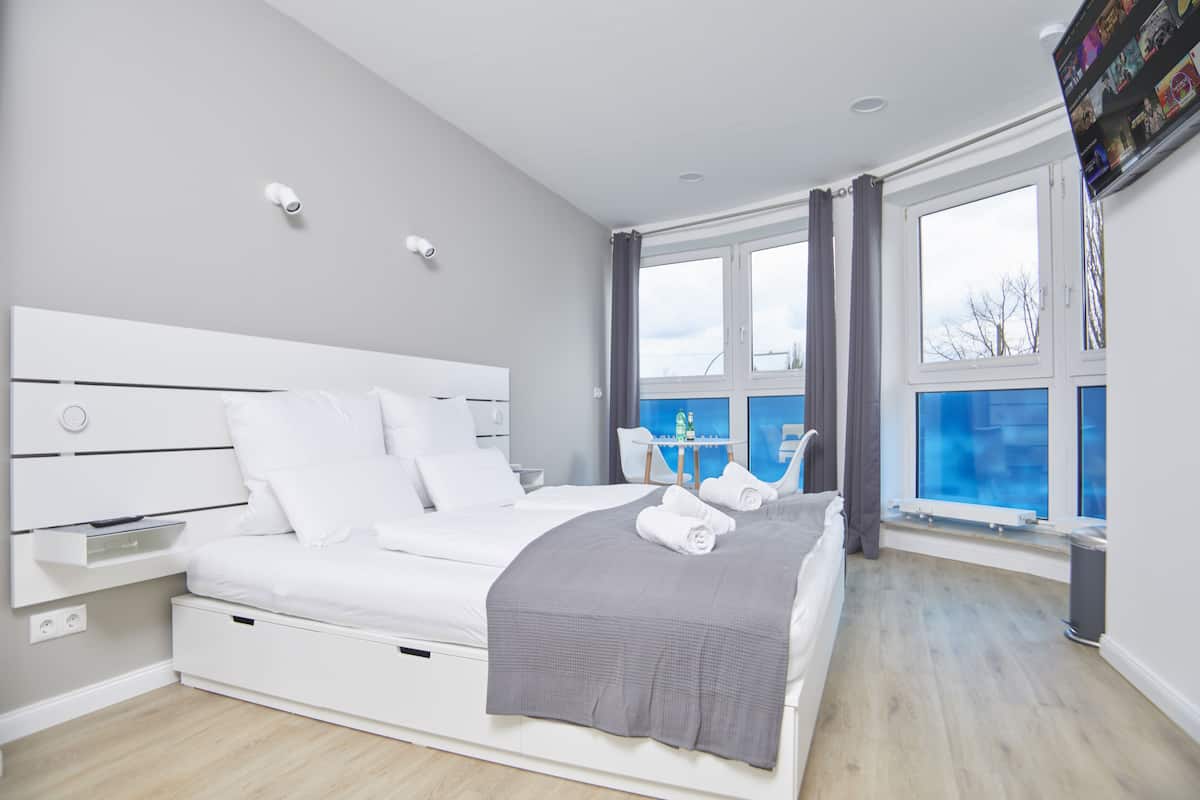 Ein modernes Schlafzimmer mit einem großen Bett, einem Nachttisch, einem Fenster mit Vorhängen und Blick ins Freie.