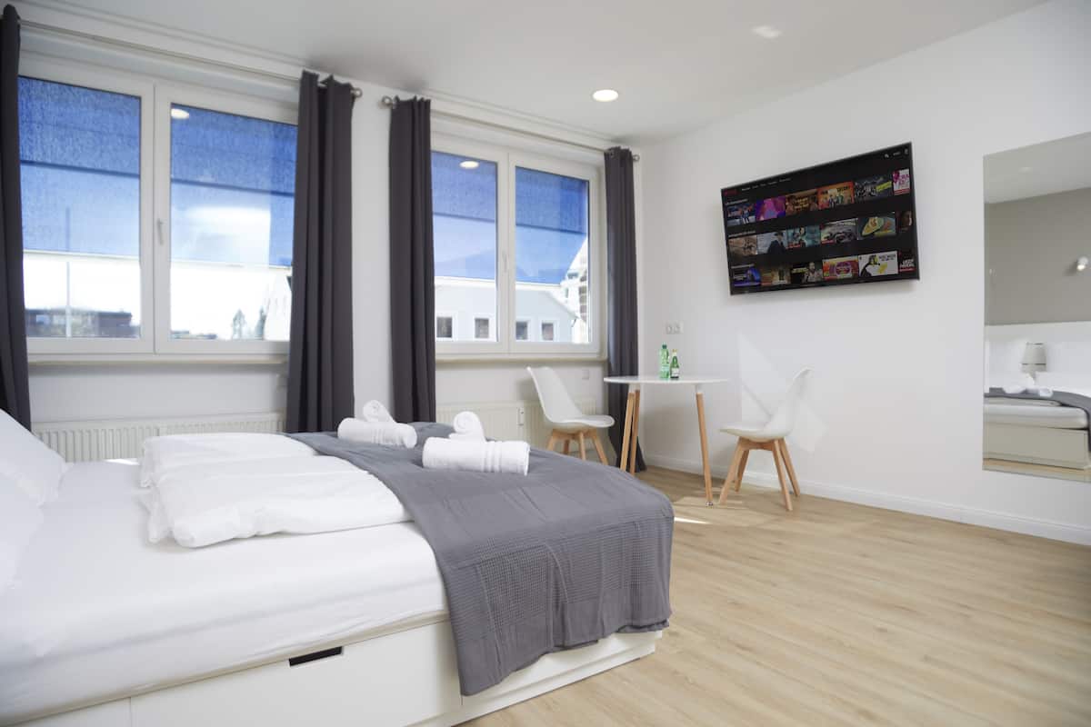 Ein modernes Hotelzimmer mit Bett, Schreibtisch, Stuhl und einem an der Wand befestigten Fernseher.